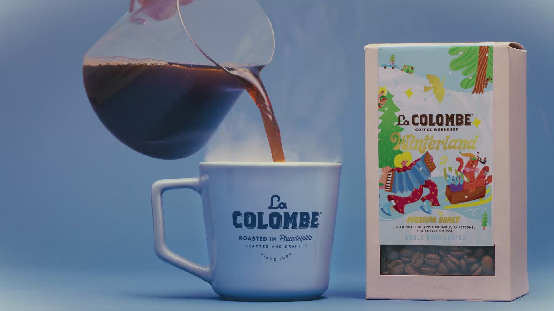 Hot coffee pouring into a mug alongside Winterland holiday blend box
